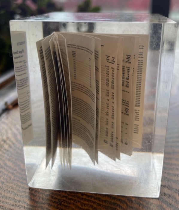 A mini prospectus encased inside a transparent vintage paperweight, sitting on a desk.